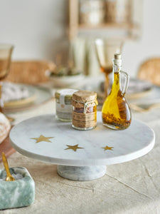 white marble cake stand with 3 brass stars imbedded holding seasoning on dining table